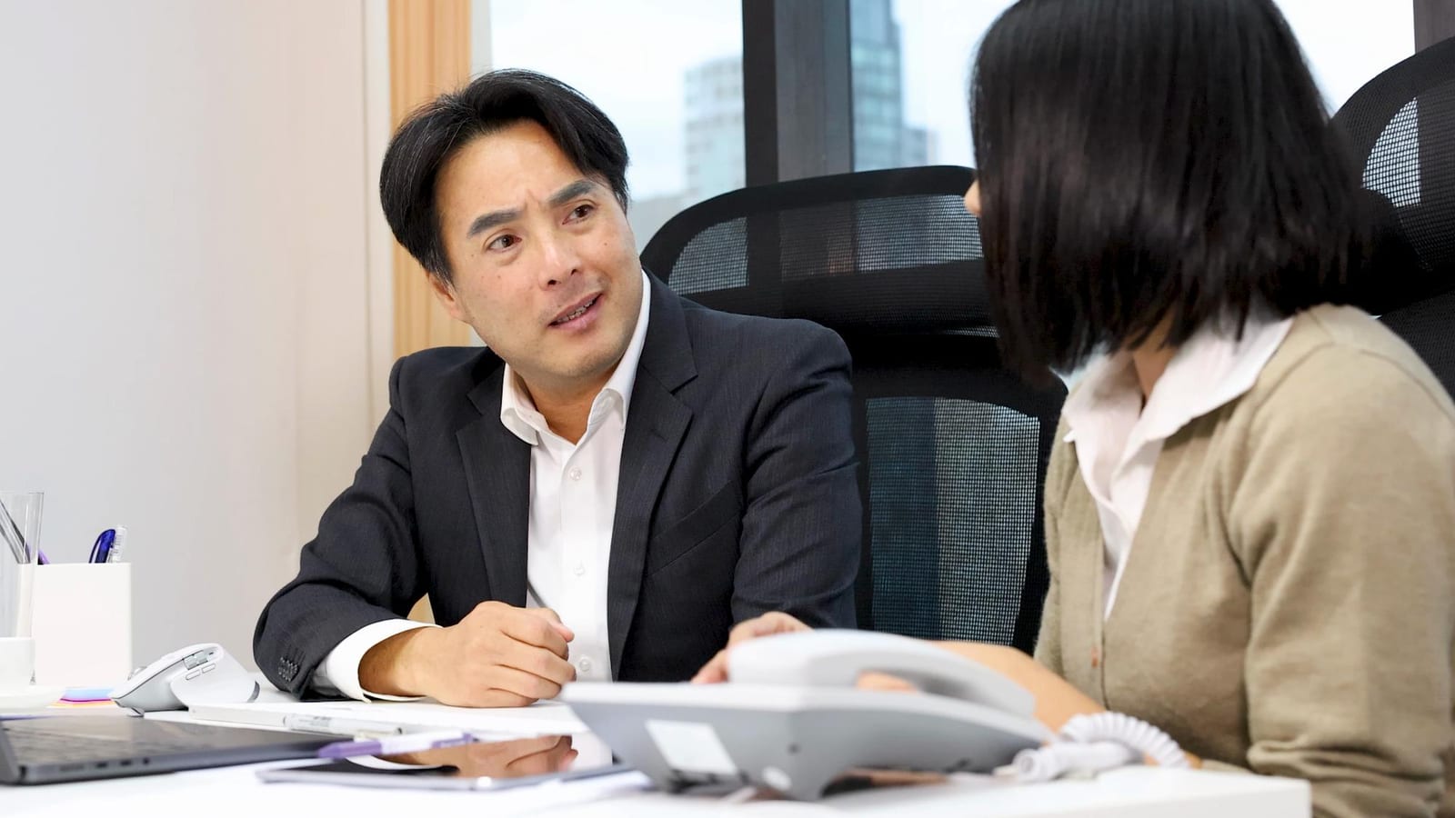 スーツ姿の日本人担当者がオフィスで同僚と講座内容について話し合う様子