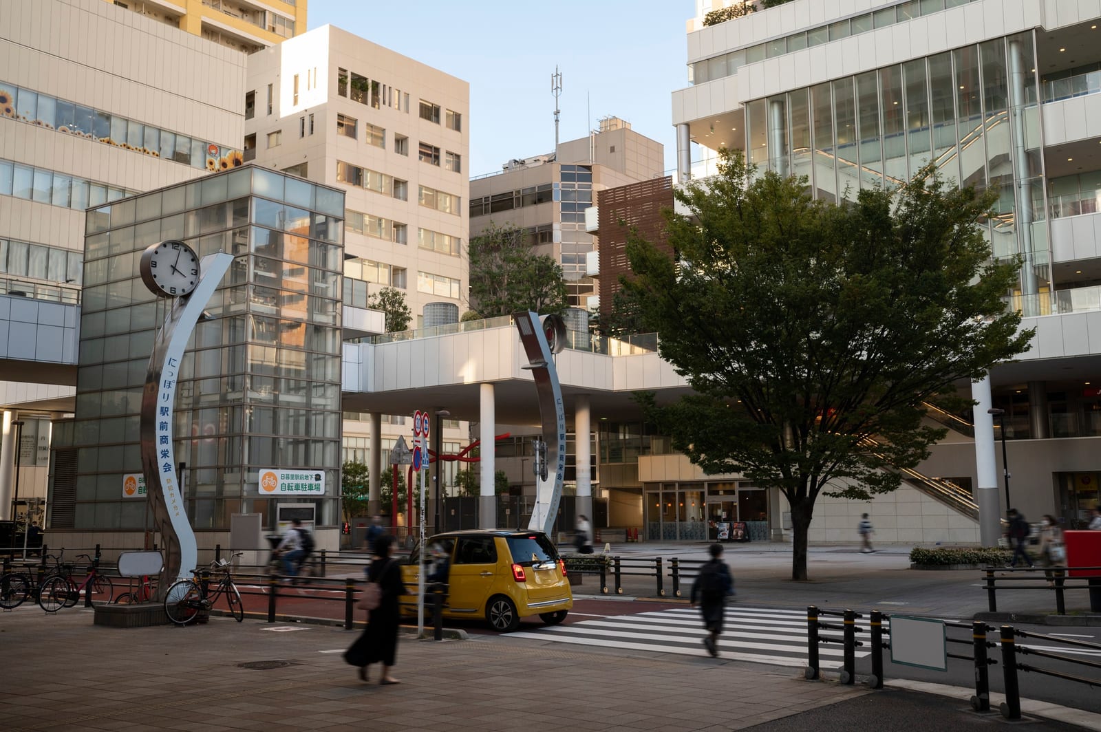 前橋市内の駅前広場を夕方に行き交う歩行者と自転車、時計塔のある風景