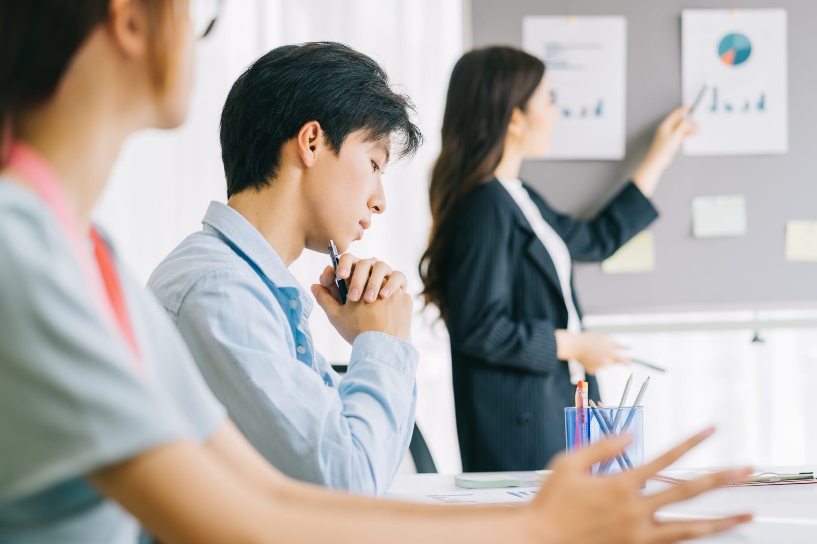 日本人男性が熱心に耳を傾け、隣の女性が壁の図表を指し示している様子