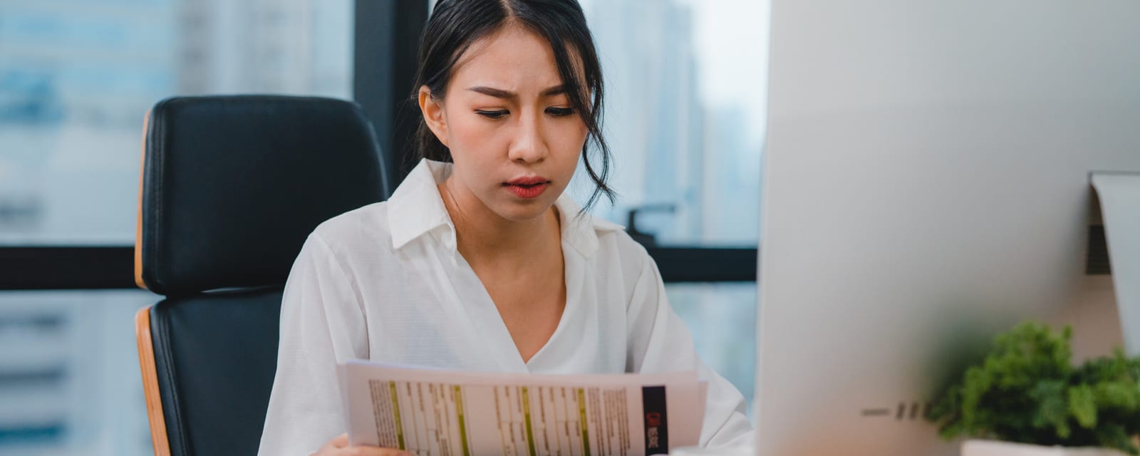 分厚い印刷資料を前に考え込む日本人女性のデスクの様子