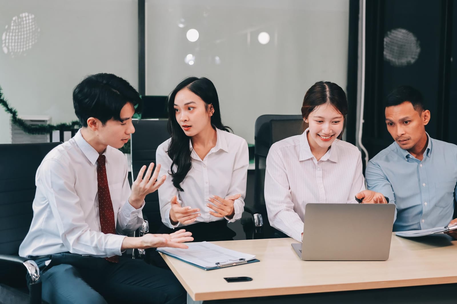 4人の日本人スタッフがノートパソコンとクリップボードを囲んで会議室で話し合う様子